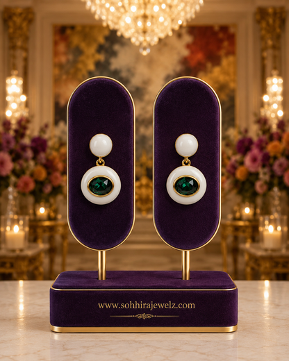 Pearl White Enamel Emerald Drop Earrings on royal purple velvet oval display stands with chandelier and floral backdrop